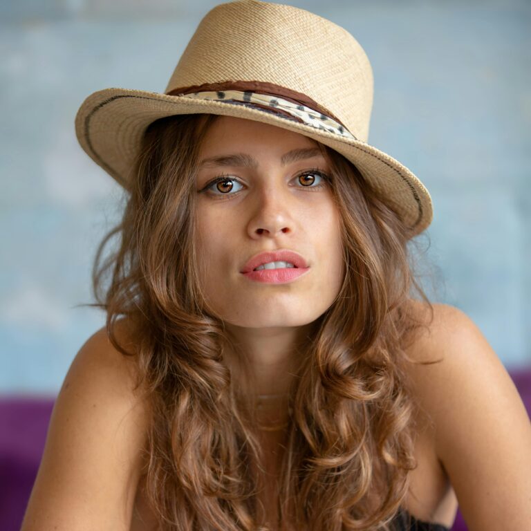 Close-up of a fashionable woman with a straw hat and curly hair, expressing a captivating look.